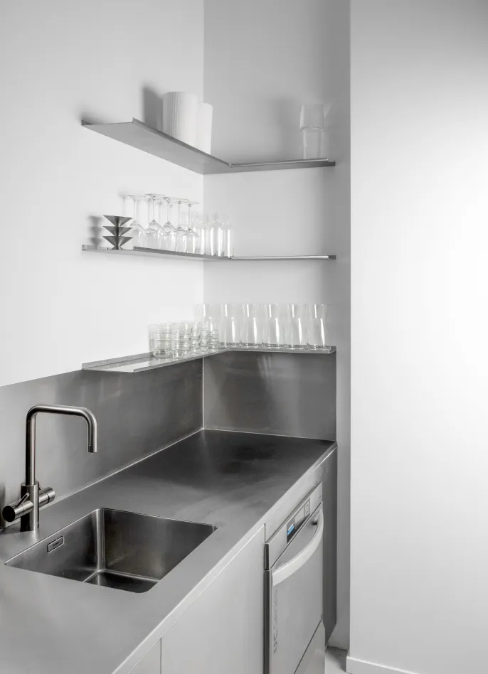 Minimalistische Küchenzeile aus Edelstahl mit integriertem Spülbecken und offenen Wandregalen mit Glaswaren im Plot Projects Popup-Space Frankfurt am Main